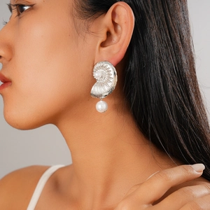 Detailed view of silver seashell texture earrings with white pearl drop on a model