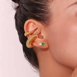 Close-up of gold hollow twist ear clips and green gemstone earrings layered on ear