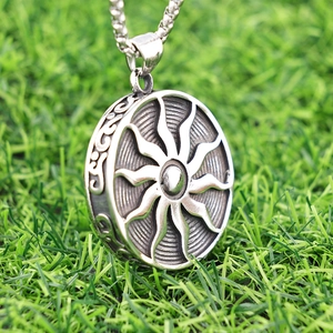 Vintage stainless steel sun totem pendant necklace on green grass with a long chain