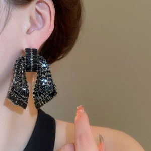 Macro detail of black ribbon bow earrings with glittering rhinestones worn by a model
