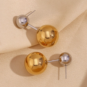 Makro-Detail minimalistischer zweifarbiger Kugelohrringe in Gold und Silber auf Satin