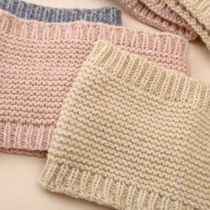 Detail of knitted baby hats and scarves set showing texture in beige, pink, and grey
