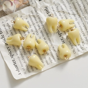 Artistic layout of multiple resin tooth charms with gold rings on vintage newsprint