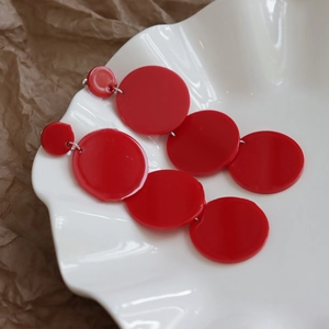 Detailed close-up of red acrylic round tassel earrings on a white ceramic display tray