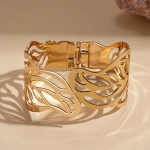 Detailed view of wide gold hollow cuff bracelet with intricate wing pattern and hinge closure