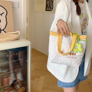 Quilted tote bag detail featuring cartoon bear embroidery and green flower charm