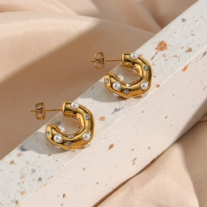 Detalle de pendientes en C dorados de 18K con perlas y cristales sobre fondo de seda