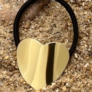 Elastic ponytail holder with polished golden heart metal charm on outdoor ground