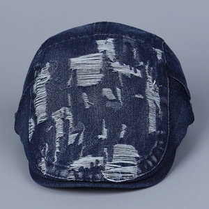 Detail of distressed dark blue denim newsboy cap featuring heavy ripped textures