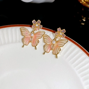 Gros plan de boucles d'oreilles papillon en émail rose doré avec perles