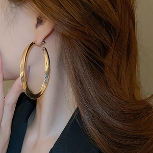Close-up of polished gold-finish oval hoop earrings worn by a fashion model