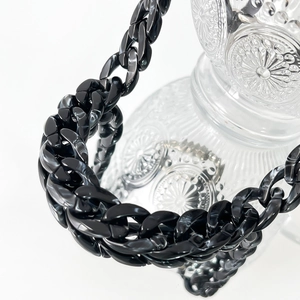 Close-up of black acrylic chunky chain links with glossy finish on a glass bottle