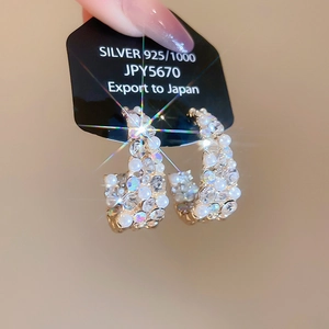 Close-up of gold-plated C-shaped earrings with faux pearls and sparkling rhinestones