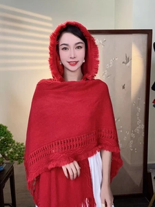 Detail of red hooded knit shawl featuring intricate openwork patterns and fringe edges