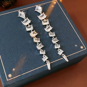 Macro detail of sparkling rectangle zircon tassel earrings on a luxury gift box