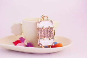 Detail of white enamel suitcase keychain with sparkling rhinestones and gold-tone metal accents
