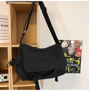 Detail view of a large black canvas messenger bag featuring a buckle closure and strap