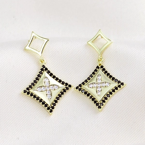 Foto macro de pendientes geométricos dorados con circón blanco y halo de diamantes negros
