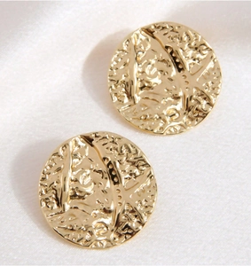 Detail view of round gold stainless steel earrings with hammered texture on silk fabric
