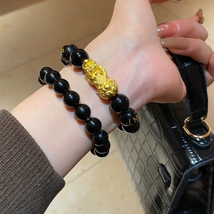 Close-up of black obsidian beaded bracelet with golden Pi Xiu charm and engravings