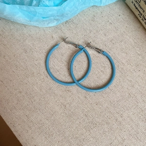 Detailed view of large minimalist blue metallic hoop earrings on textured fabric