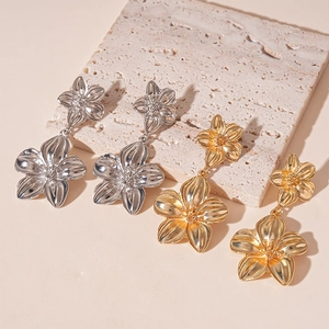Elegante goldene und silberne metallische Blumenohrringe auf einer strukturierten Steinplatte