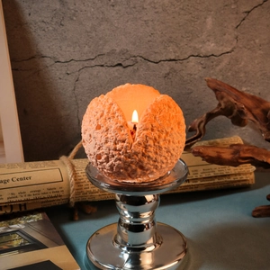 Candela sferica con texture a cratere arancione su supporto in metallo argento e fiamma