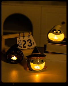 Three ceramic Halloween tea light candle holders with pumpkin and ghost designs in a cozy setting