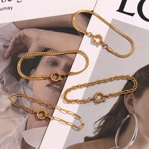 Flat lay of four 18K gold plated stainless steel chain bracelets on a magazine