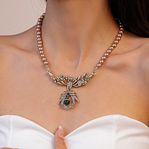 Detail of vintage beaded necklace with gold engraved spider pendant and green gemstone