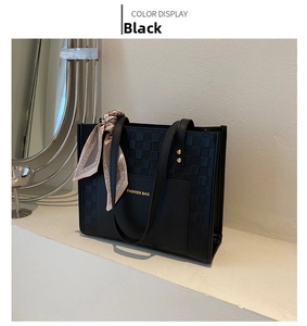Detail of black tote bag with checkered texture, silk scarf, and gold fashion lettering