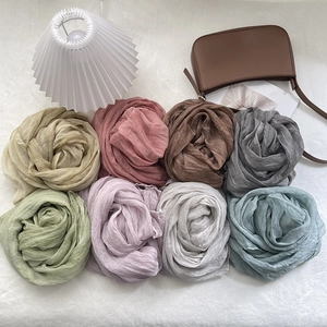 Assorted pleated silk scarves in soft pastel tones arranged with elegant lifestyle props