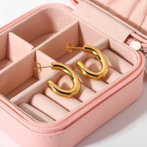 Gros plan de créoles dorées en forme de C présentées dans un écrin à bijoux rose