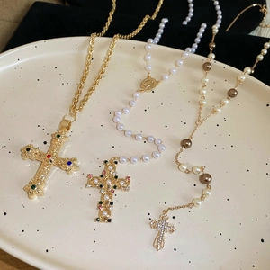 Close-up of gold cross pendants on pearl and chunky chain necklaces in a ceramic tray