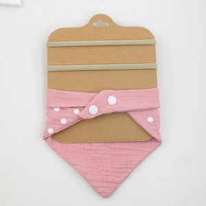 Detailed set featuring a pink polka dot cotton bib and two beige elastic headbands