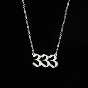 Vue macro du collier avec pendentif chiffre 333 argenté sur un fond noir minimaliste