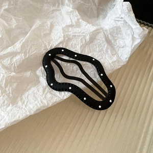 Detail of black wavy hair clip with white polka dots on elegant textured background