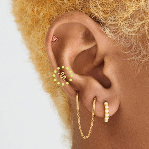 Close-up of golden snake stud and pearl hoop earrings set worn on ear cartilage
