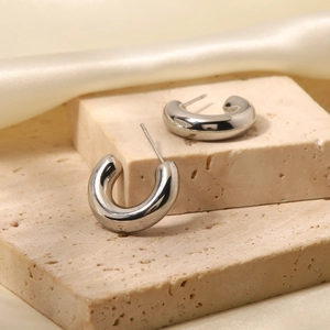 Detailed view of silver C-shaped titanium steel earrings on natural stone and silk texture