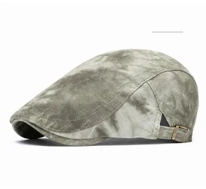 Detail view of tie-dye flat cap featuring an adjustable bronze buckle on green fabric