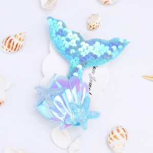 Detail of blue sequined mermaid tail hair clip with pearlescent sea stars on white card