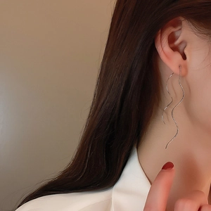 Close-up of silver wavy tassel ear thread earrings worn on a model's ear