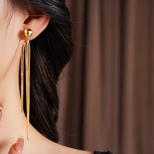 Detailaufnahme langer goldener Quastenohrringe an einem Model mit metallischem Glanz