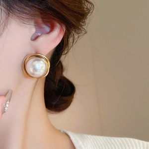 Close-up of elegant round pearl earrings with spiral gold wire wrap on model's ear