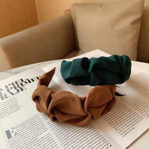 Gros plan de serre-têtes plissés vert foncé et caramel sur un magazine de mode