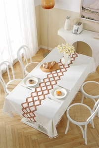 Detail of cream tassel tablecloth with geometric embroidery and fringe on wooden table