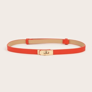 Detail of slim orange leather belt featuring a classic gold metal twist lock buckle