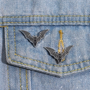 Detail of gothic black enamel bat brooches pinned on a light blue denim jacket pocket