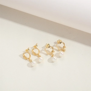 Detailed view of geometric golden earrings set with white pearls on a textured background
