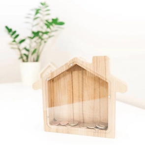 Macro shot of house-shaped oak wood money box with clear acrylic panel and coins inside